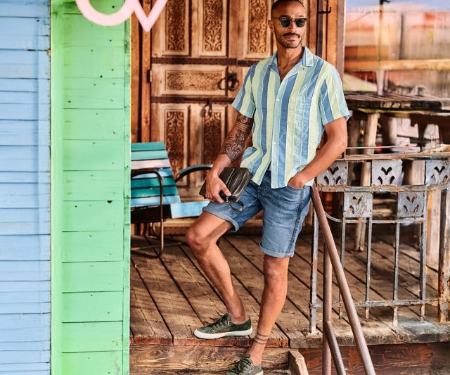 Mann in gestreiftem Kurzarm-Hemd mit hellblauer Jeansshorts und grünen Sneakern