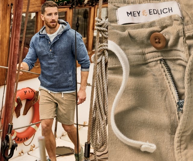 Mann in blauem Kapuzen-Pulli mit beiger Shorts und grünen Sneakern