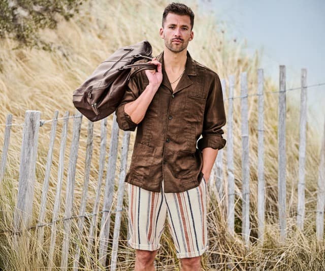 Ein Mann trägt ein braunes Hemd und gestreifte Shorts und hält eine Tasche über der Schulter.
