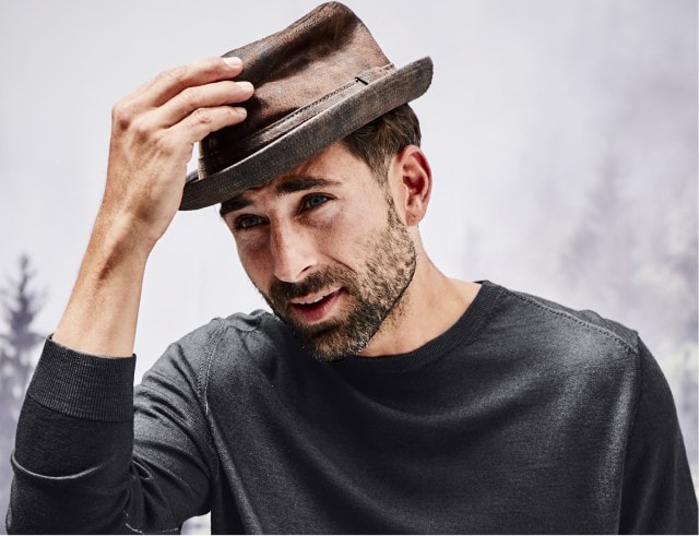 Mann der einen braunen Trilbyhut trägt vor einem neutralen Hintergrund