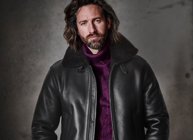 Mann in rotem Pullover und Lederjacke vor einem neutralen Hintergrund
