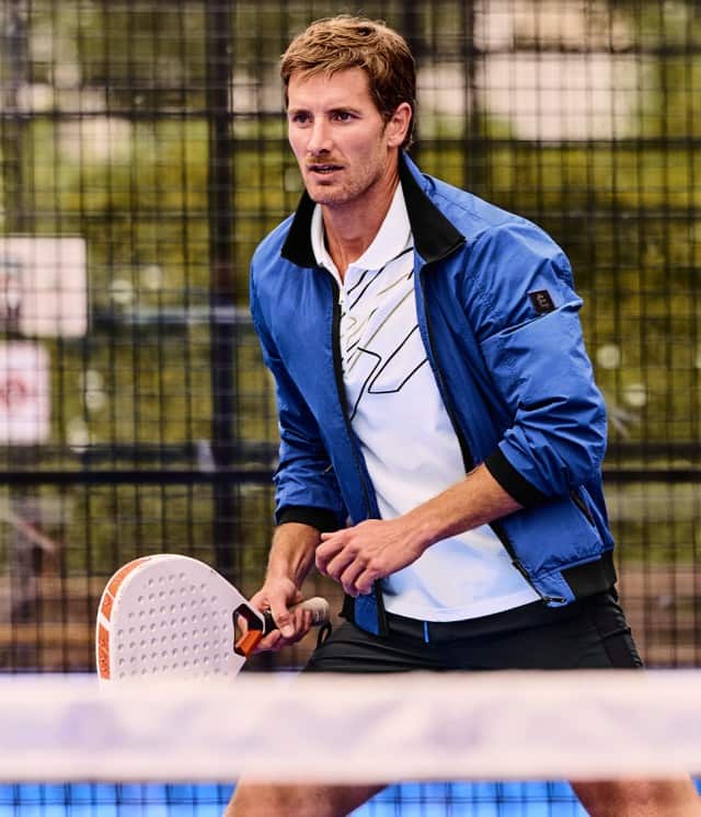 Ein Mann spielt konzentriert Padel und hält dabei ein Padel‑Racket in der Hand, während er in sportlicher Kleidung auf den nächsten Ball vorbereitet ist.