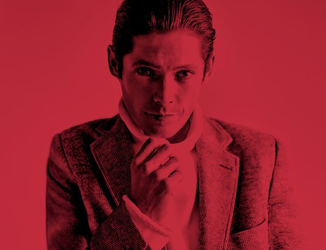 Das Bild zeigt einen elegant gekleideten Mann vor einem komplett roten Hintergrund, der als aufmerksamkeitsstarke Sale‑Inszenierung dient.