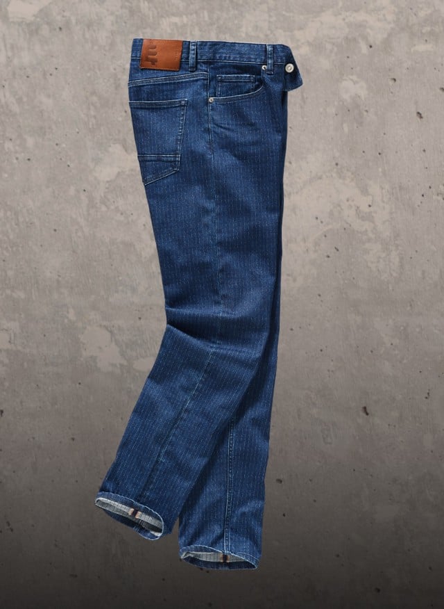 Auf dem Bild ist eine blaue Jeans mit feiner vertikaler Streifenstruktur zu sehen, einmal im Detail und einmal in voller Länge vor einer Betonwand.