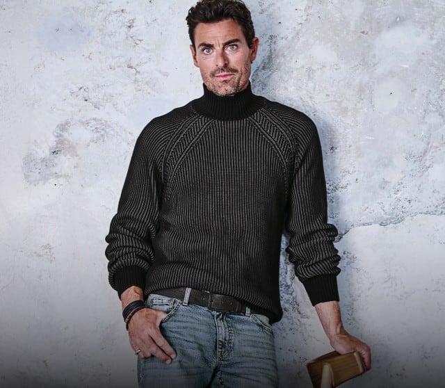 Ein Mann trägt einen dunkelgrauen, gerippten Rollkragenpullover, kombiniert mit einer hellen, verwaschenen Jeans.