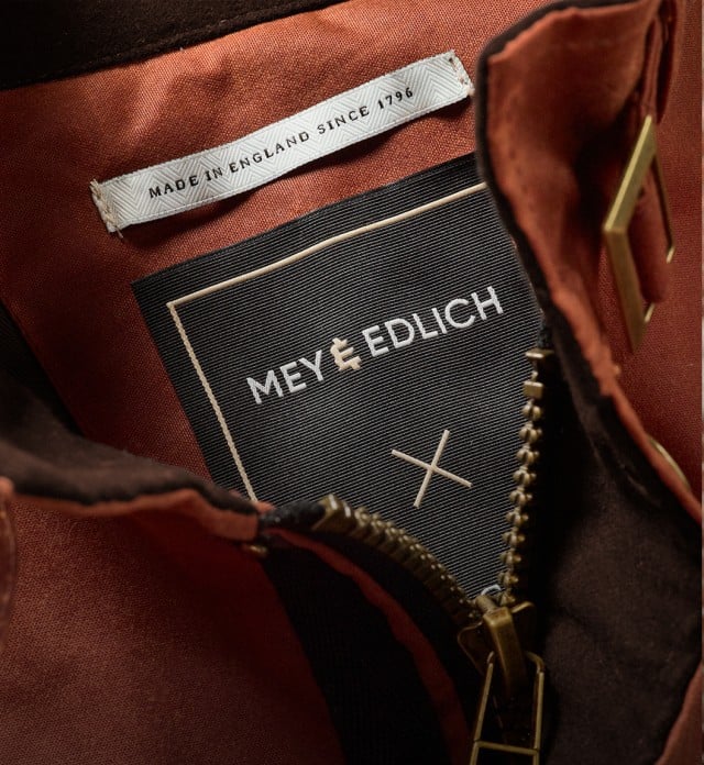 Der Mann trägt eine rostrote Fieldjacket über einem hellblauen Pullover und einer dunkel strukturierten Hose.