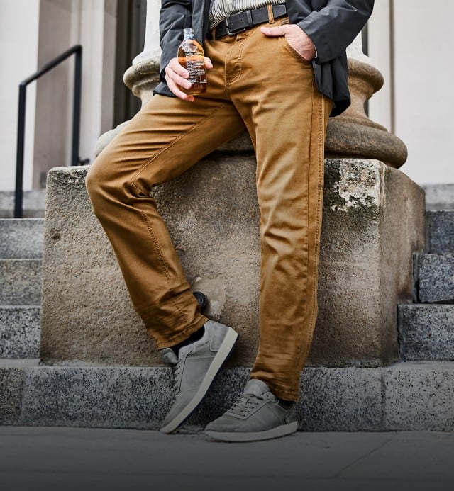 Der Mann trägt eine senfgelbe Hose und graue Sneaker.