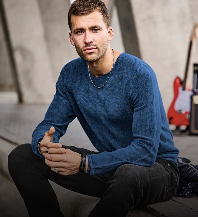 Ein Mann trägt einen blauen, strukturierten Strickpullover und eine dunkle Jeans.