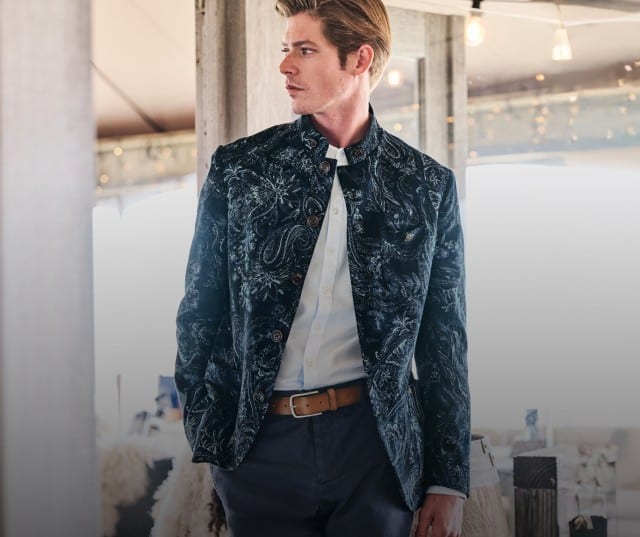 Ein Mann in einem blauen Cordsakko und einem weißen Hemd blickt neugierig zur Seite.