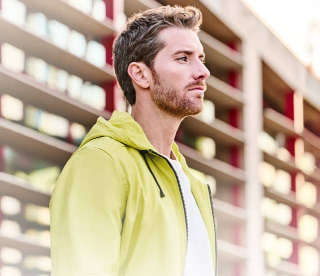 Ein Mann bekleidet mit einer gelben Lederjacke steht vor einem Sichtschutzzaun