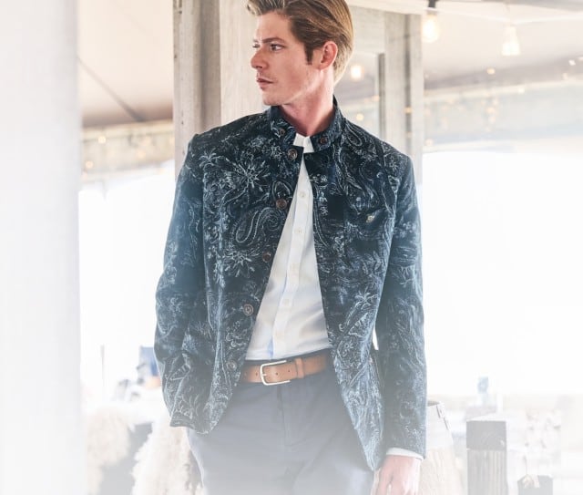 Das Bild zeigt einen Mann in einem blau gemusterten Sakko der sich durch eine moderne Wohnung bewegt.