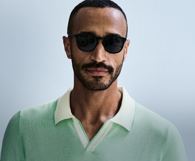Ein Mann trägt ein mintfarbenes Poloshirt und eine dunkle Sonnenbrille und blickt frontal in die Kamera.