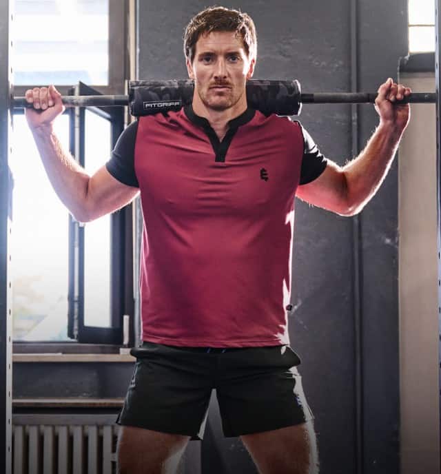 Auf dem Bild ist ein Mann in einem Sportoutfit zu sehen der im Fitnessstudio mit Gewichten trainiert.
