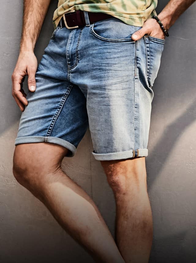Ein Mann in Jeansshorts lehnt lässig an einer grauen Wand.