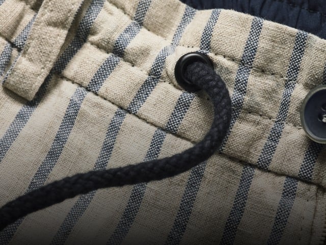 Eine detaillierte Nahaufnahme zeigt den gestreiften Bund einer Stoffhose mit Kordelzug, während rechts daneben die gleiche gestreifte Shorts freigestellt im Ganzen vor hellem Hintergrund dargestellt ist.