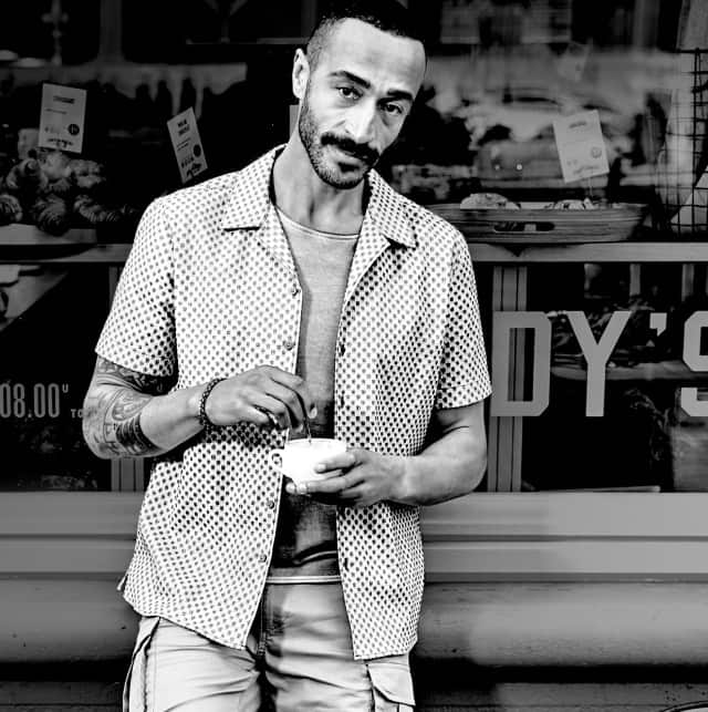 Eine Schwarz Weiß Aufnahem von einer Person die vor einem Cafè steht und eine Tasse in der Hand hält