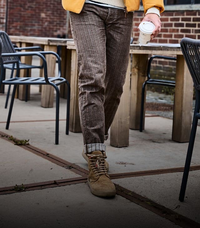 Der Look zeigt braune Cordhosen, lässig hochgekrempelt und kombiniert mit beigen Wildlederboots – ein stilvolles, herbstliches Ensemble mit rustikalem Charme.