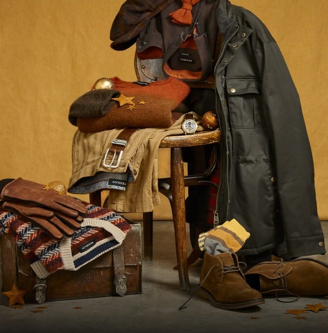 Das Bild zeigt eine dekorativ arrangierte Auswahl an herbstlich‑winterlicher Kleidung und Accessoires vor einem warmen Hintergrund.