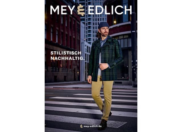 Auf dem Cover ist ein Mann zu sehen, der in einer städtischen Abendkulisse einen dunkel karierten Mantel, eine beige Hose, dunkle Schuhe und eine blaue Mütze trägt.