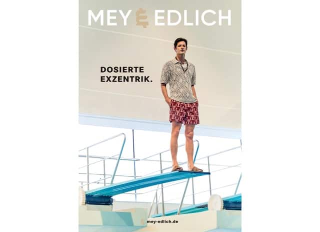 Auf dem Cover steht ein Mann in gemustertem Hemd und roten Shorts entspannt auf einem Sprungbrett über einem Pool.
