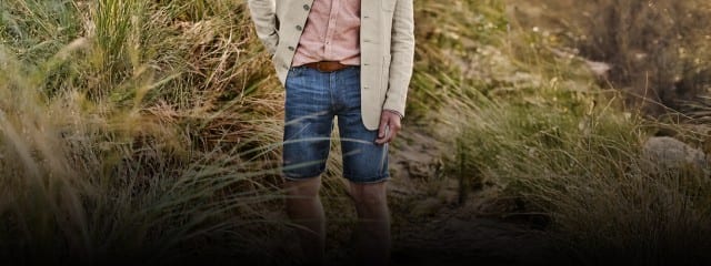 Beige Leinenweste über rosafarbenem Hemd, kombiniert mit umgekrempelten Jeansshorts und braunem Gürtel. Lässiger, sommerlicher Stil.
