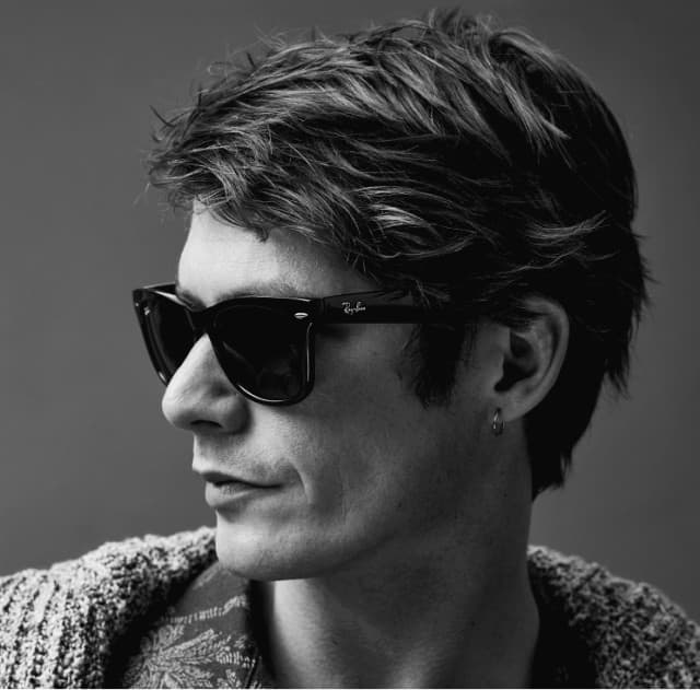 Strickjacke über einem gemusterten Oberteil, kombiniert mit einer markanten Sonnenbrille. Lässiger Vintage-Stil.