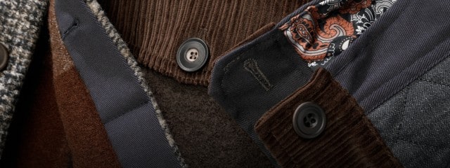 Die Nahaufnahme zeigt verschiedene Stoffmaterialien und -muster, darunter Cord, Wolle und gemustertes Futter, mit Knöpfen und Nähten im Detail.