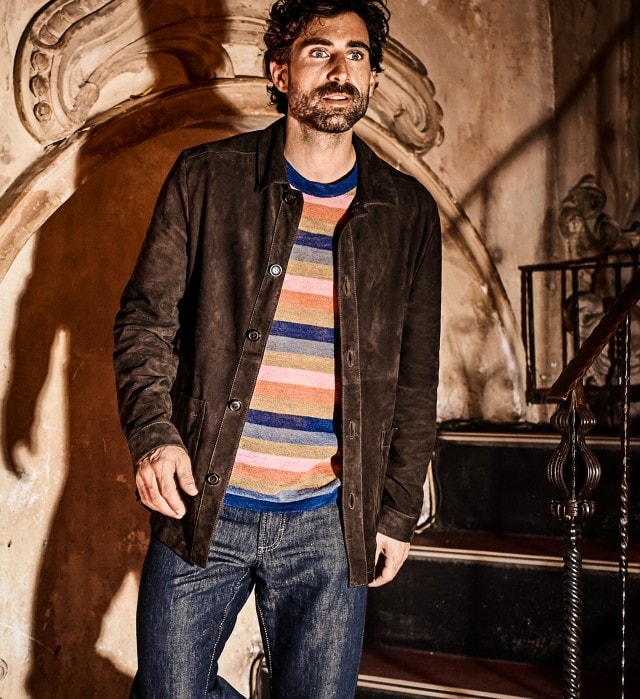 Mann mit brauner Lederjacke und gestreiftem Pullover geht eine Treppe hinunter