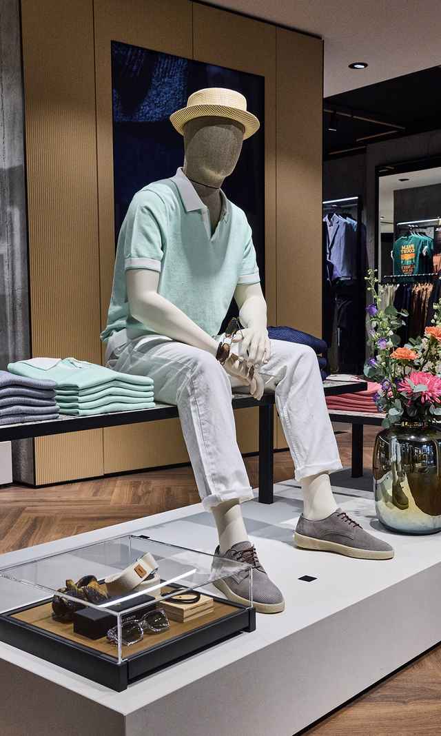 Das Bild zeigt die neu gestaltete M&E Filiale mit einer sitzenden Schaufensterpuppe in sommerlichem Outfit, dekorativer Warenpräsentation und stilvollen Accessoires auf einem zentralen Podest.