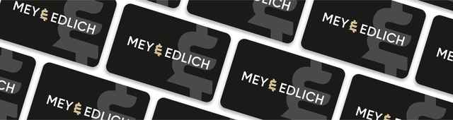Auf dem Bild sind mehrere schwarze Karten mit dem weißen Schriftzug „MEY & EDLICH“ und dem Mey und Edlich Logo im Hintergrund in einem versetzten Muster angeordnet.