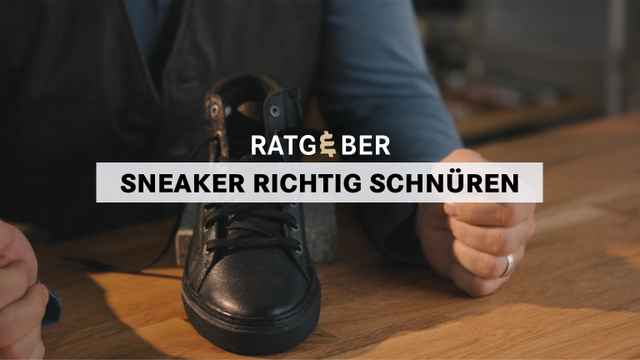 Person hält schwarzen Sneaker auf Holztisch, Text: "Ratgeber Sneaker richtig schnüren".