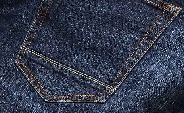 Das Bild zeigt eine Nahaufnahme von dunkelblauem Denimstoff mit einer aufgesetzten Gesäßtasche und kontrastierenden, orangefarbenen Nähten.