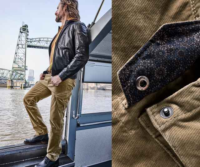 Ein Mann trägt eine schwarze Lederjacke über einem senfgelben Oberteil und kombiniert dazu eine sandfarbene Cordhose mit Cargotaschen und schwarzen Schnürschuhen.