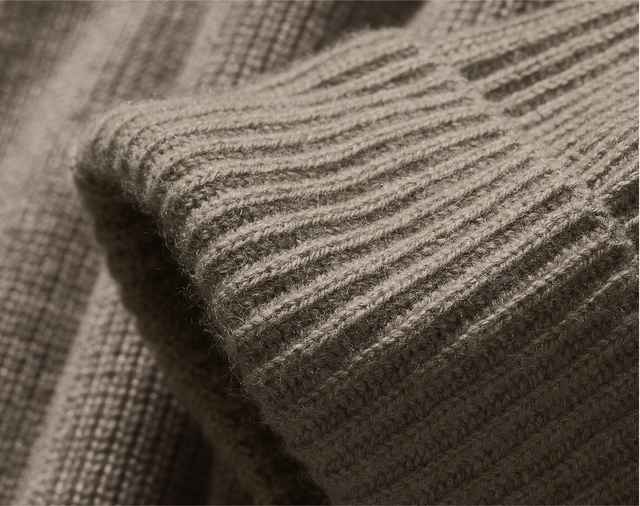 Auf dem Bild ist eine Nahaufnahme eines gerippten, flauschigen Strickstoffs in einem warmen Beigeton zu sehen, vermutlich der Ärmel eines Pullovers.