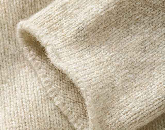 Das Bild zeigt eine Nahaufnahme eines weichen, grob gestrickten Wollstoffs in hellem Beigeton, der eine warme und natürliche Textur erkennen lässt.