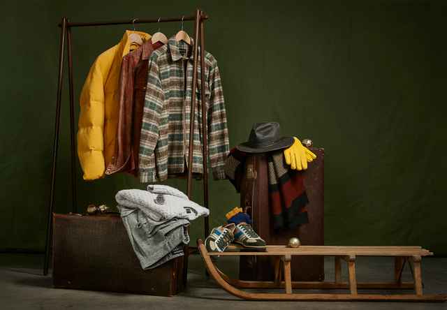 Das Bild zeigt eine stilvoll arrangierte Wintergarderobe mit Jacken, Accessoires und einem Holzschlitten.