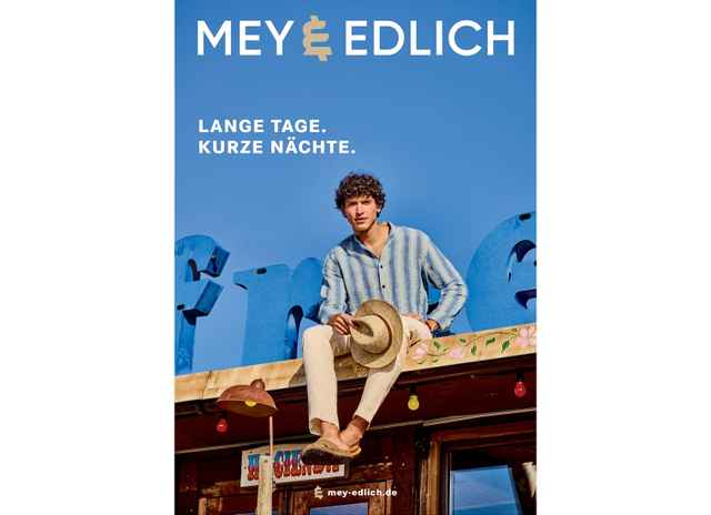 Ein Mann sitzt auf einem Dach vor blauem Himmel und hält einen Hut. Text: "Lange Tage. Kurze Nächte." Markenname oben.