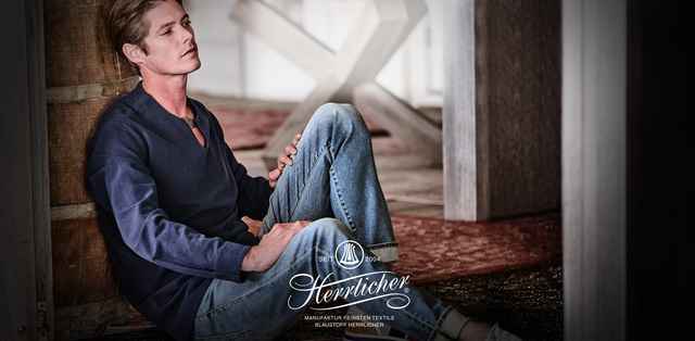 Ein Mann bekleidet mit einer Jeans und einem blauen Hemd sitzt nachdenklich auf dem Boden