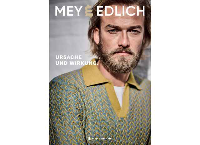 Mann mit Bart trägt gemusterten Pullover mit gelbem Kragen, während er auf ein Plakat für Mey & Edlich schaut. Text: "Ursache und Wirkung."