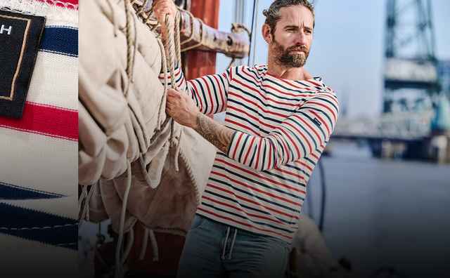 Ein Mann trägt ein gestreiftes Shirt und hält ein Seil auf einem Boot; links ist das Etikett von MEY & EDLICH x SAINT JAMES zu sehen.
