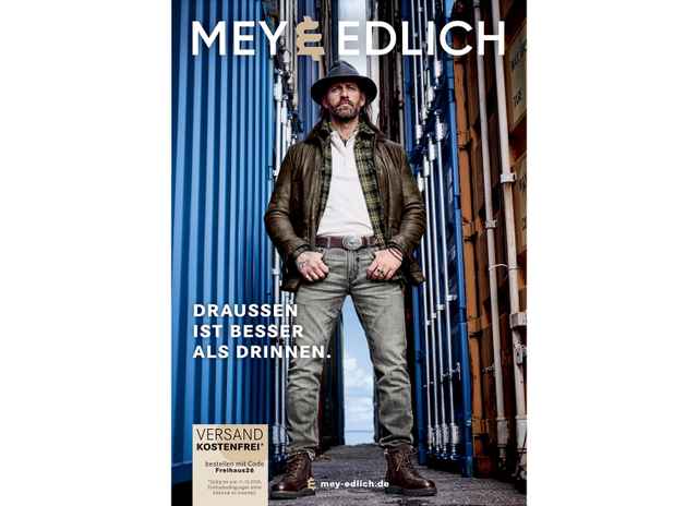 Mann in Outdoor-Kleidung mit Hut steht zwischen blauen und braunen Containern. Text: "Draußen ist besser als drinnen". Mey&Edlich Logo.