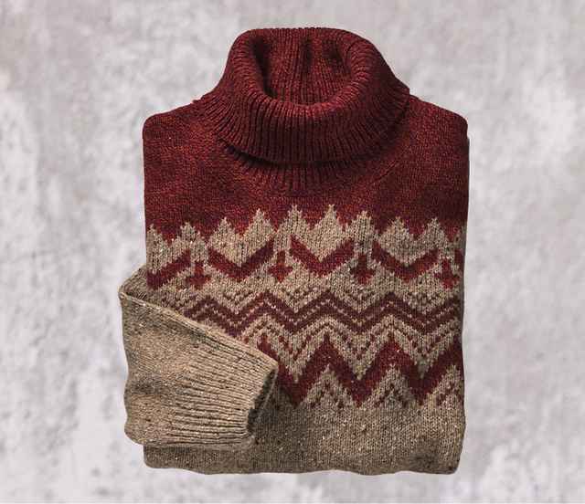 Roter Rollkragenpullover mit Zickzackmuster in Creme und Braun, sorgfältig gefaltet, auf einem grauen Hintergrund platziert.