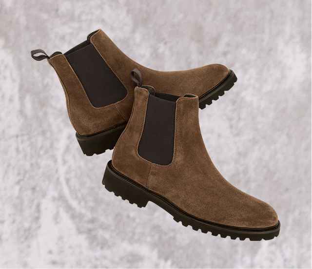 Ein Paar braune Chelsea-Stiefel mit seitlichen Gummieinsätzen und Profilsohle auf grauem Hintergrund.