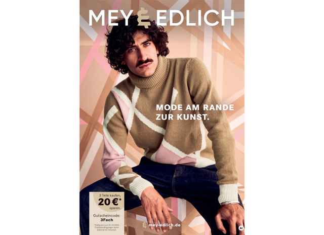Mann mit lockigem Haar und Schnurrbart trägt einen gestrickten Pullover in Braun und Pastelltönen, lehnt sich vor geometrischem Hintergrund.