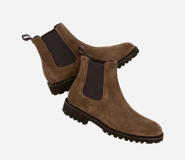 Ein Paar braune Chelsea-Stiefel aus Wildleder mit schwarzem elastischem Einsatz und robuster Profilsohle auf weißem Hintergrund.